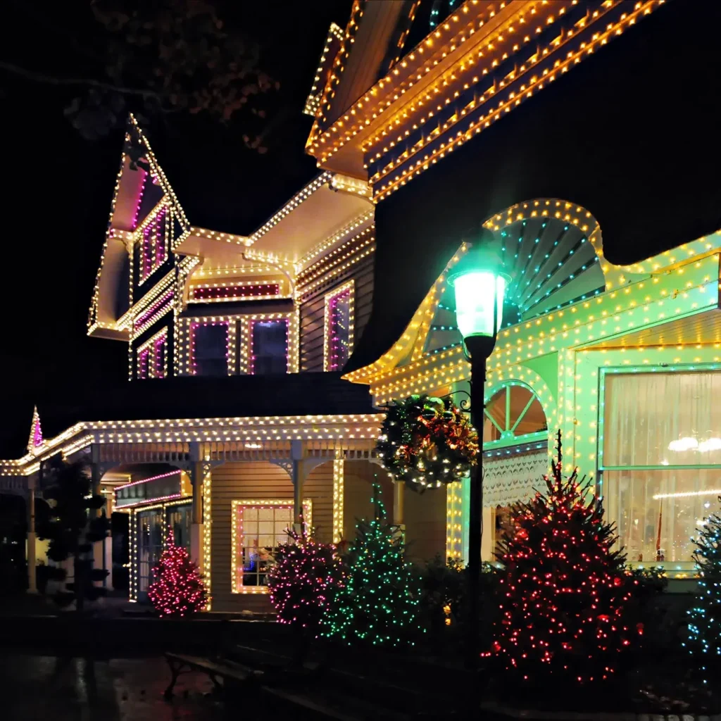 Victorian home with warm white Christmas lights outlining the rooflines and windows, and colorful lights on the front yard trees