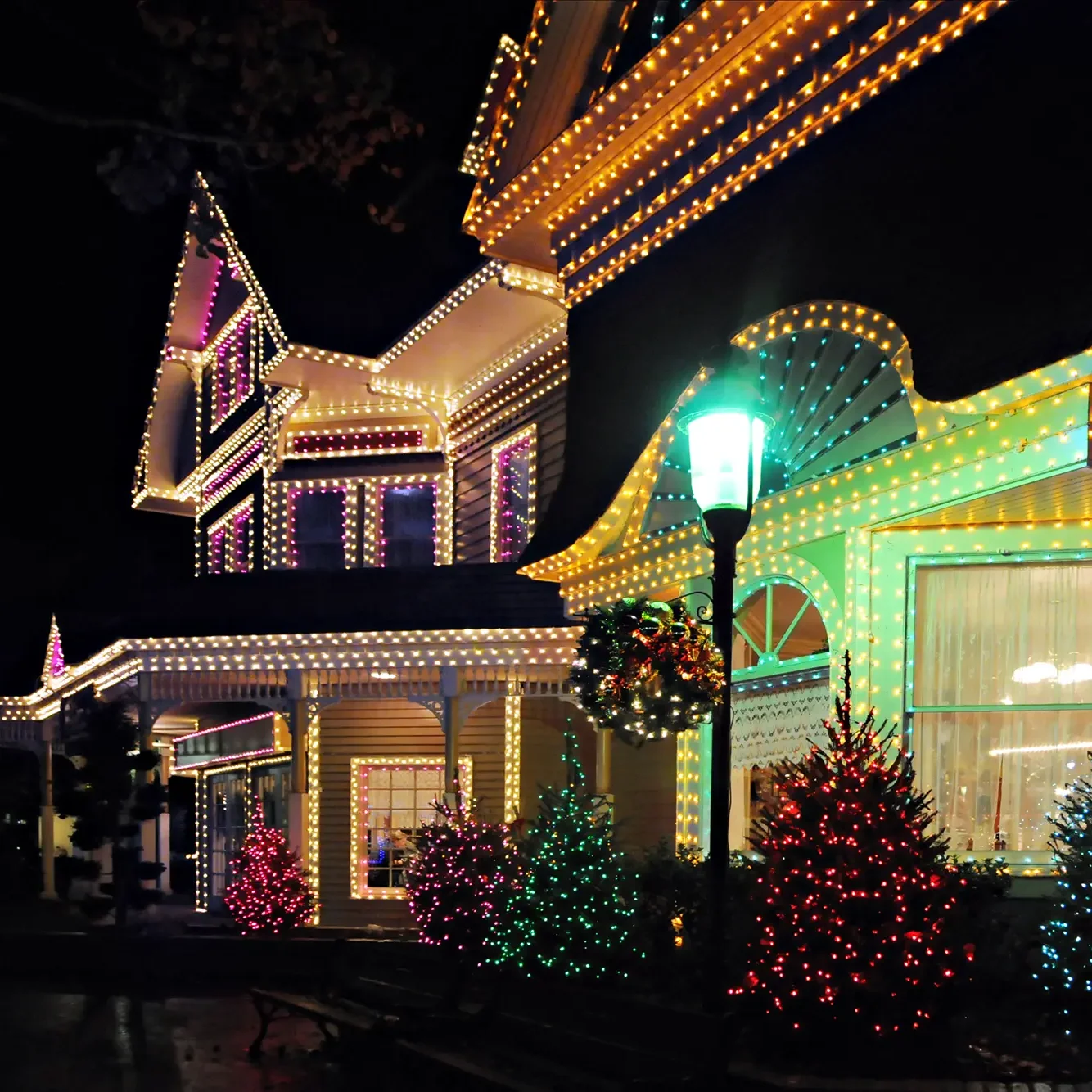 Victorian home with warm white Christmas lights outlining the rooflines and windows, and colorful lights on the front yard trees